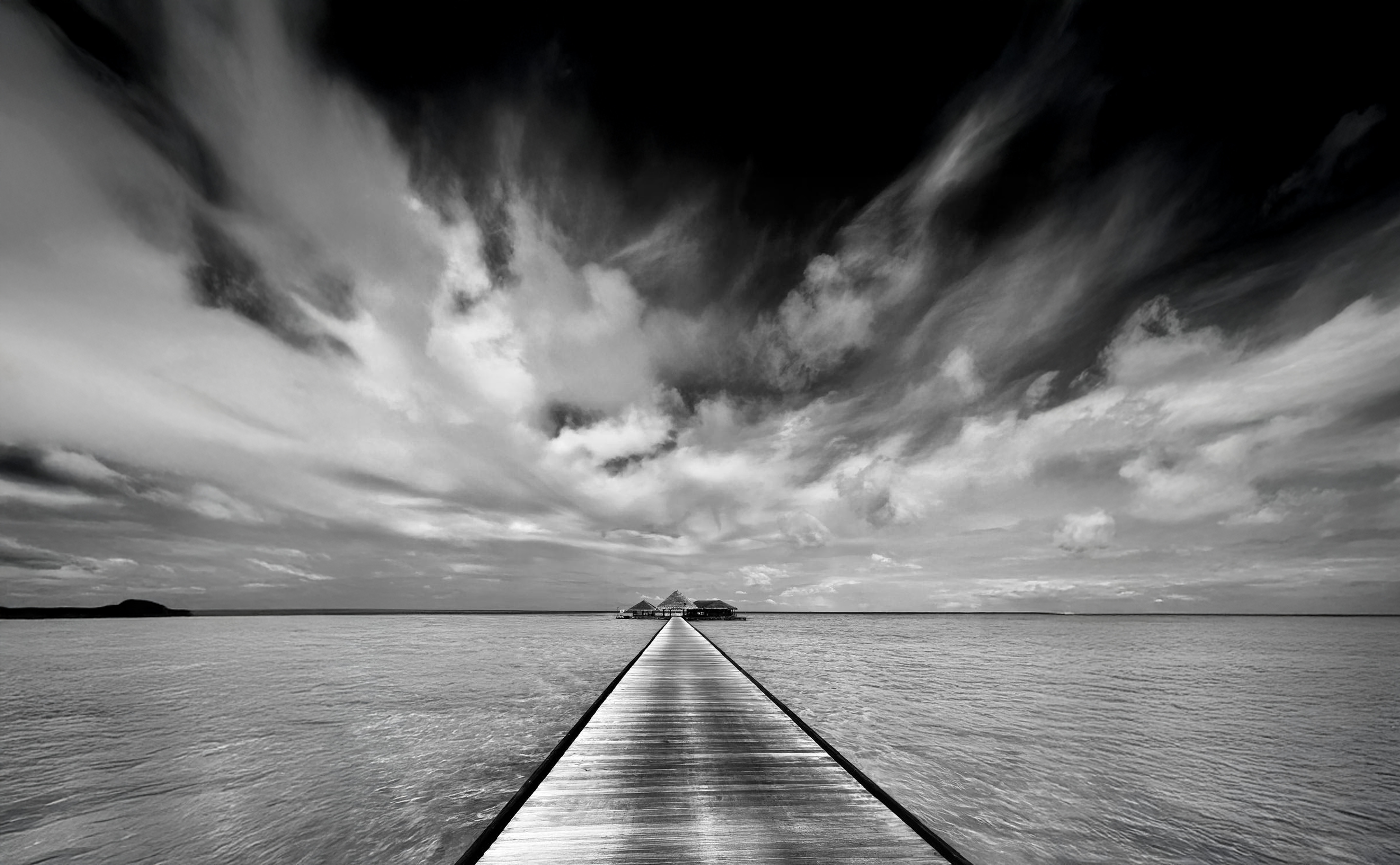 Black and white photograph of a pier leading across water in the Maldives