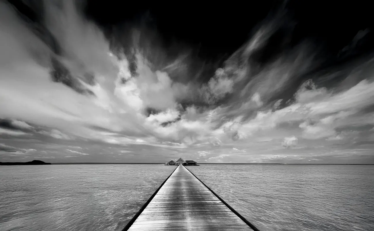 Black and white photograph of a pier leading across water in the Maldives
